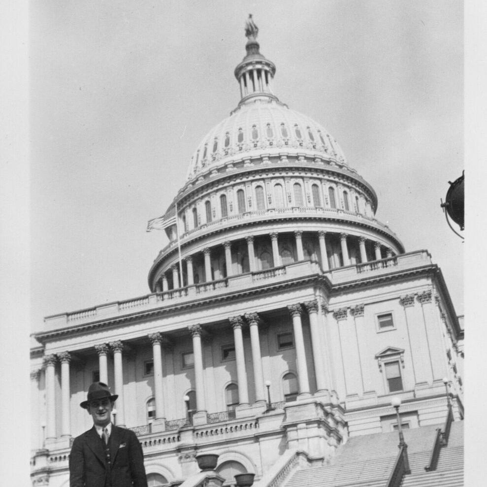 LBJ in hat and suit standing on the steps of the U.S. Capitol, with the dome behind him